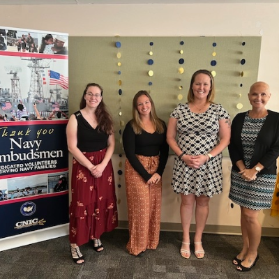 A picture of four female volunteer Ombudsmen standing next to a banner thanking Navy Ombudsmen.